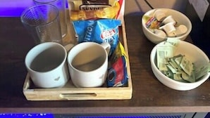 A tray with two cups, a bag of chips, and a bowl of cash on a wooden surface.