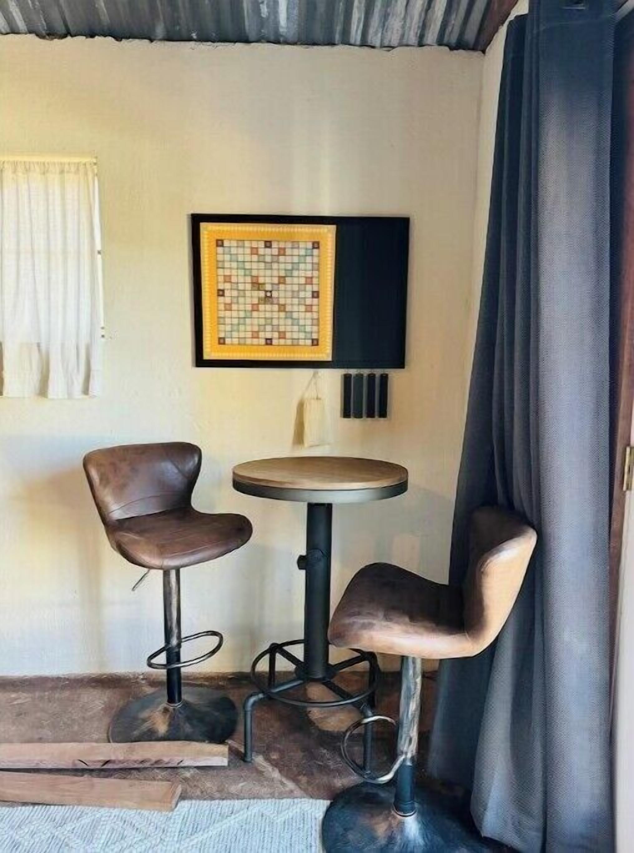 A corner room with two bar stools, a small round table, and a framed puzzle on the wall.