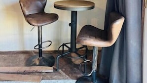 A corner room with two bar stools, a small round table, and a framed puzzle on the wall.