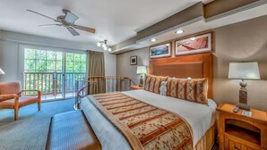 Une chambre d’hôtel avec un grand lit, un ventilateur de plafond, un balcon avec une chaise et une tête de lit en bois.