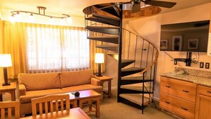 Un espace de vie compact comprenant un escalier en colimaçon, un canapé, une table à manger et un coin cuisine.