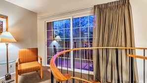 Une chambre d’hôtel avec un escalier en bois aux courbes élégantes, une grande fenêtre avec des rideaux, une chaise et une lampe.