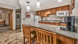 A kitchen with granite countertops, wooden cabinets, a microwave, a refrigerator, and a coffee maker.