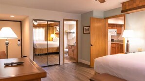 A hotel room with a bed, a desk, a chair, a kitchenette, and a bathroom.