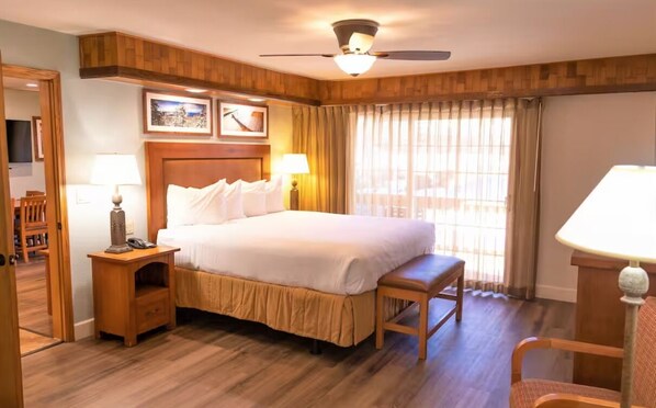 Ein Hotelzimmer mit einem großen Bett, einem Holzkopfbrett, zwei Nachttischen mit Lampen, einer Holzbank und einem Deckenventilator.