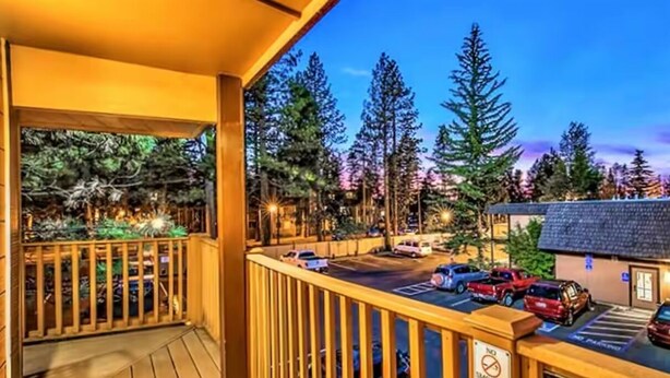 A wooden deck with a view of a parking lot and trees.