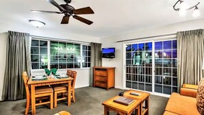 A hotel room with a dining area, a sofa, a TV, and large windows.