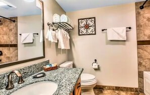 Ein Badezimmer mit einer Granit-Arbeitsplatte, einem Waschbecken, einer Toilette und einem Handtuchhalter mit mehreren Handtüchern.
