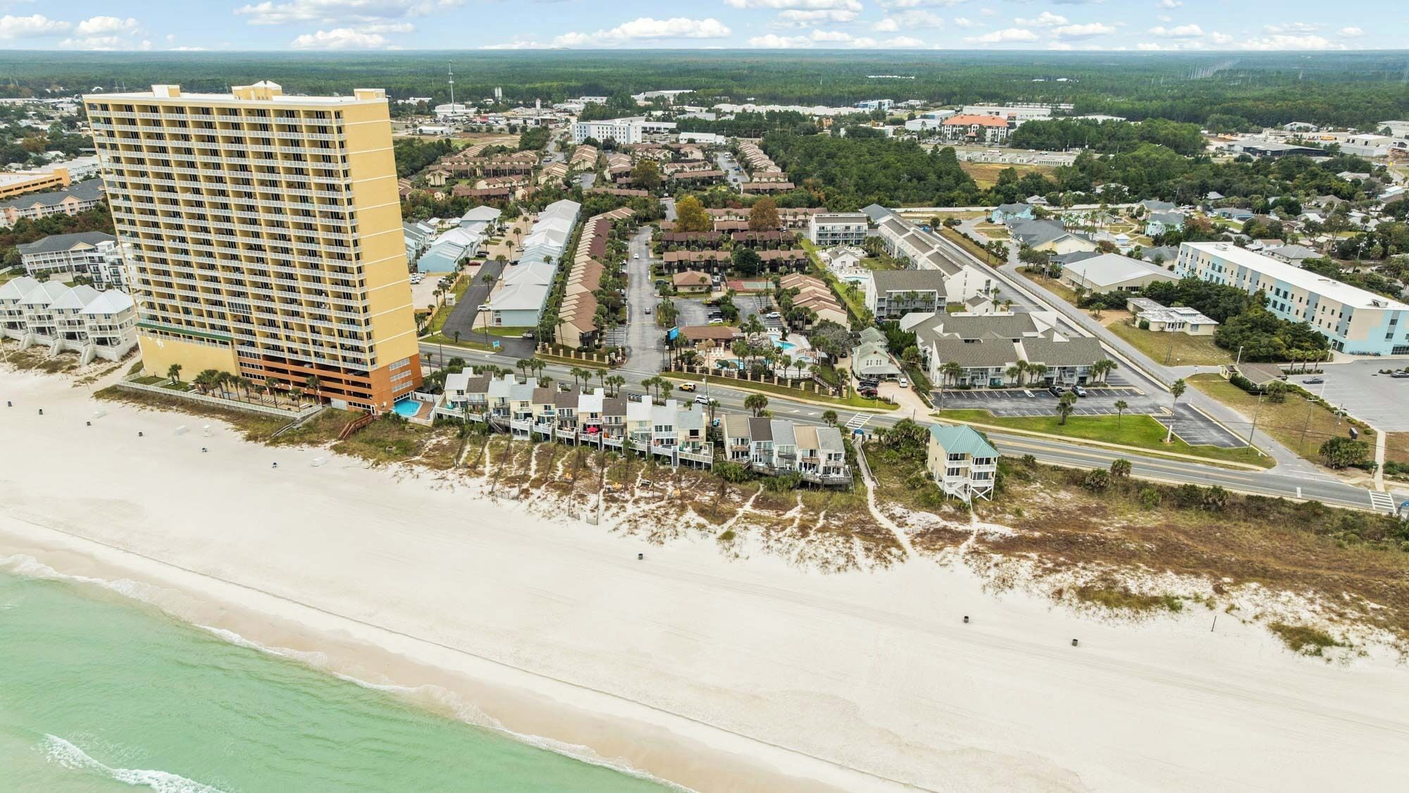 An aerial view of a coastal town with a prominent high-rise hotel, beachfront properties, and a mix of residential and commercial buildings.