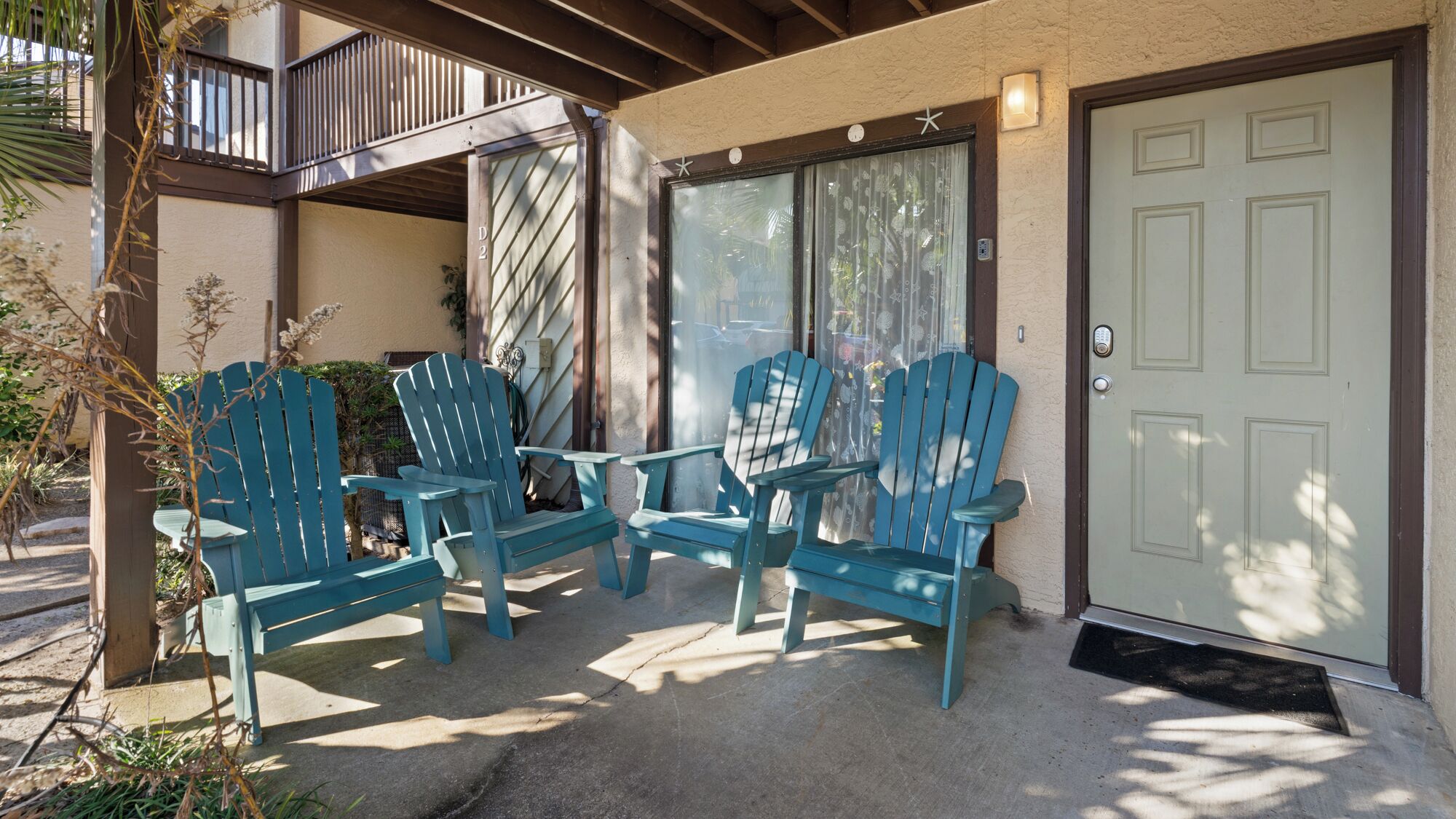 Un espace extérieur abrité, aménagé avec quatre chaises Adirondack bleues et un sol en béton.
