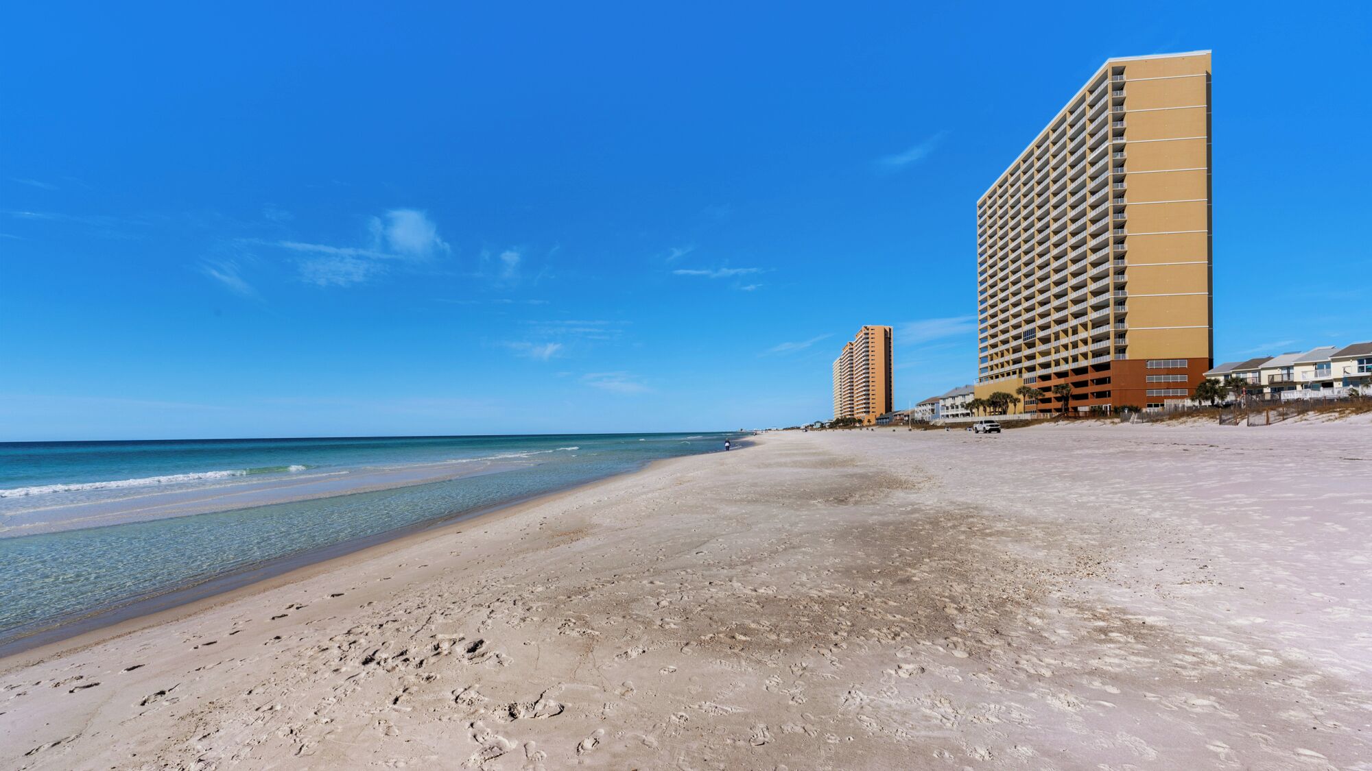 Une plage avec un rivage sablonneux, un ciel bleu dégagé et deux immeubles de grande hauteur en arrière-plan.