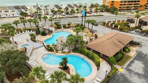 A resort with a large swimming pool, a beach view, and a parking area.