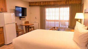 Ein Hotelzimmer mit einem großen Bett, einem an der Wand montierten Fernseher, einem Esstisch mit Stühlen und einem fenster mit Vorhängen.
