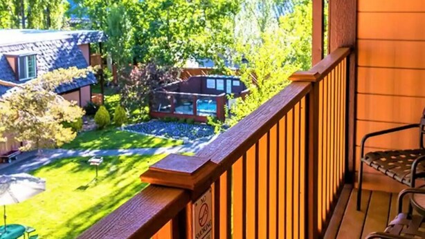 Ein Holzbalkon mit Blick auf einen Garten und benachbarte Häuser.
