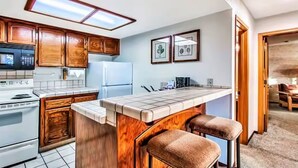Eine Küche mit Holzausstattung, einer zentralen Kochinsel mit Barhocker, einer Mikrowelle, einem Herd, einem Kühlschrank und einer Deckenleuchte.