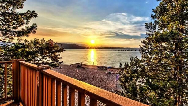 Eine Holzterrasse mit Blick auf einen Strand und einen Sonnenuntergang.