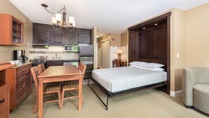 A compact hotel room with a kitchenette, a dining area, and a bed. - Deluxe Studio | Murphy Bed + Sofa (West Dover)