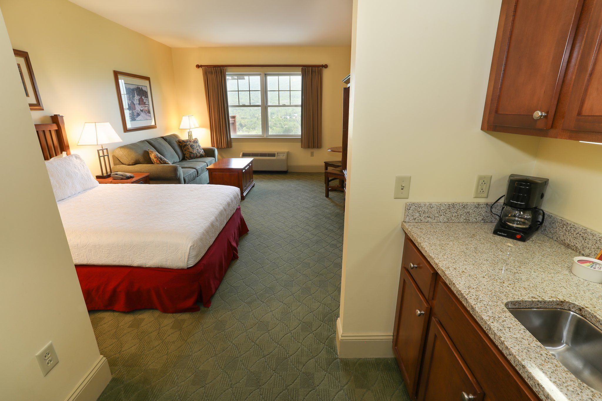 A hotel room with a bed, a sofa, a small table, a coffee maker, and a sink.