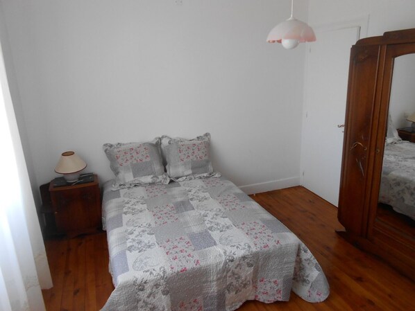 Un dormitorio con cama, mesita de noche, lámpara, espejo y suelo de madera.