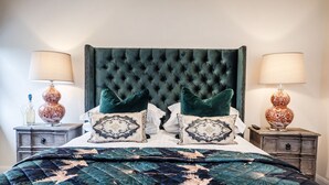 Une chambre à coucher avec une tête de lit capitonnée, deux tables de chevet avec des lampes, un lit recouvert d’une couette à motifs floraux et agrémenté de coussins décoratifs.