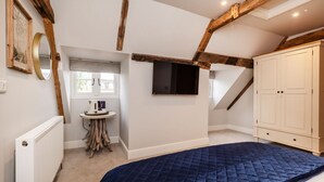 Une chambre avec un plafond en pente, un lit, une commode, un téléviseur, une petite table avec une bouilloire et une fenêtre.