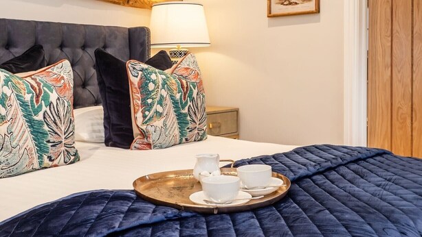 Une chambre dotée d’un grand lit, d’une poutre en bois au plafond, d’une table de chevet avec une lampe et d’une décoration murale sur le thème des tropiques.