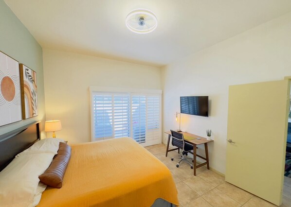 A hotel room with a bed, desk, chair, and a television on the wall.