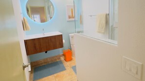 A bathroom with a round mirror, a sink, a toilet, and a glass shower enclosure.