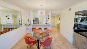 A modern kitchen with a central island, a dining area with orange chairs, and a large mirror on the left wall.