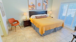 A bedroom with a bed, two bedside tables, a nightstand, a chair, and artwork on the wall.