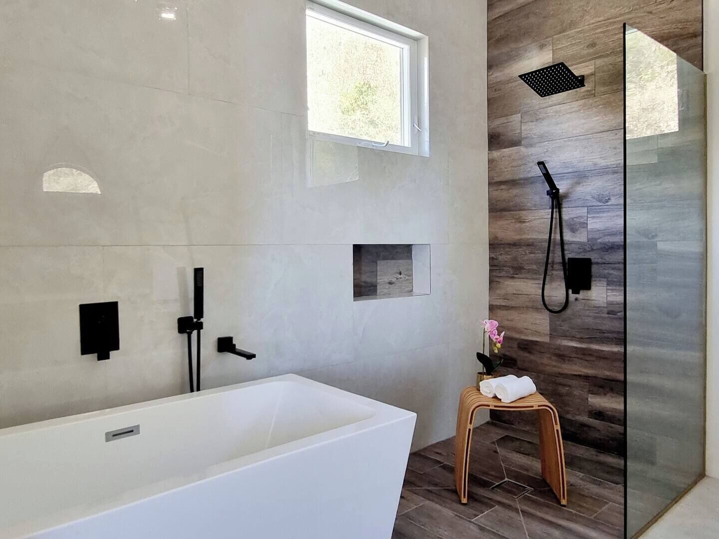 A modern bathroom with a freestanding bathtub, a glass shower enclosure, and a small wooden stool with towels.