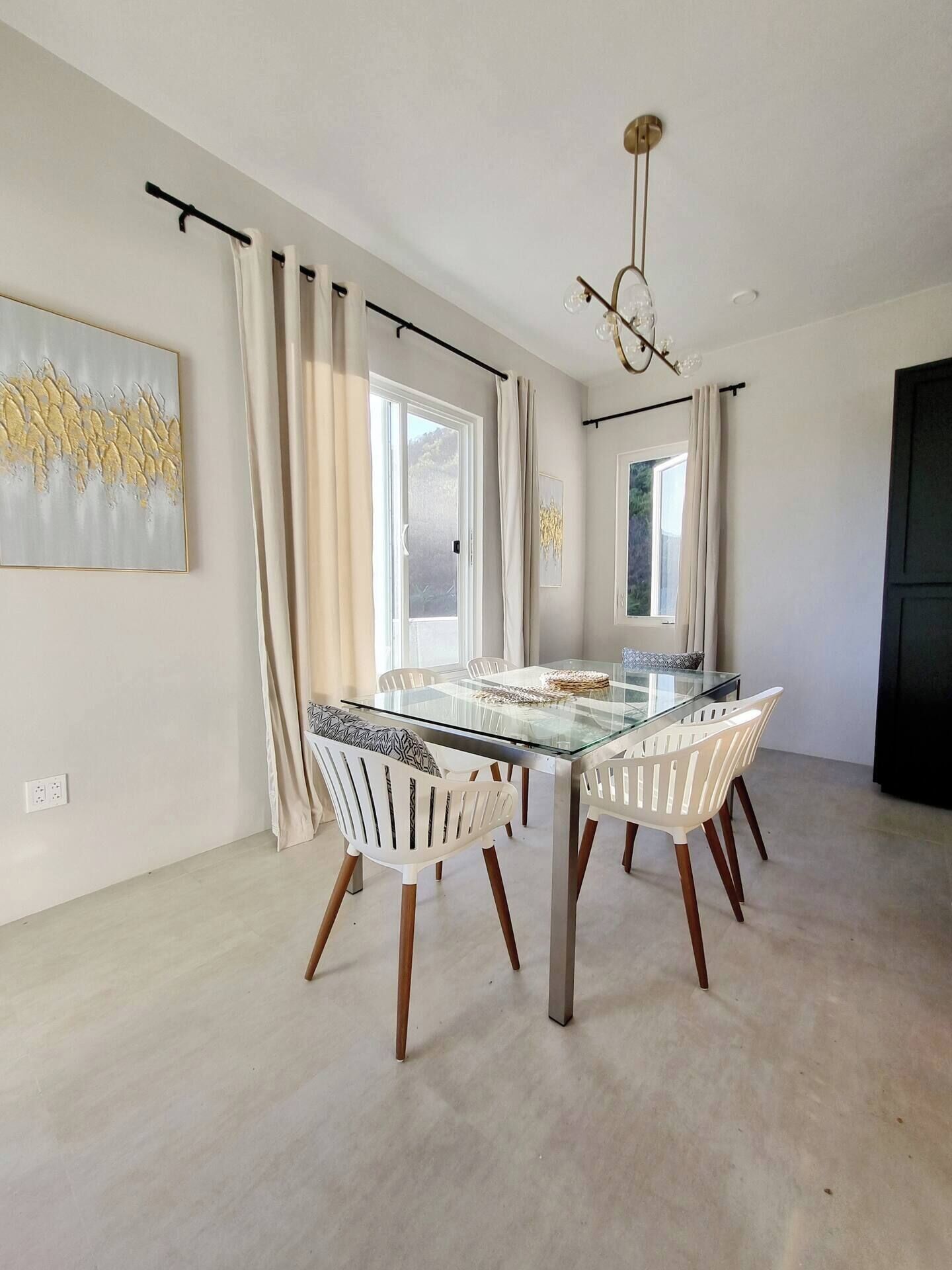 A dining area with a glass table and white chairs, a chandelier, and a painting on the wall.