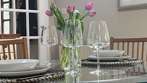 A dining table with a glass top, surrounded by chairs, a vase with flowers, and empty wine glasses. - Burn Cottage - A Secluded Highland Retreat For Two (Fortingall)