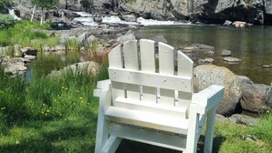 A white Adirondack chair in a grassy area with a river and forest in the background. - Fossen Camping Fagernes (Innlandet)