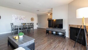 Amplia sala de estar con televisor de pantalla plana, chimenea, comedor con sillas y una mesa de centro.