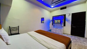 Quarto com cama, uma pequena escrivaninha, cadeira, televisão fixada na parede e porta.