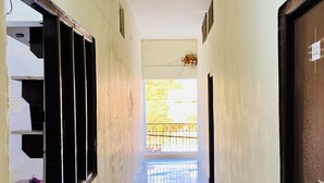 Corredor comprido e estreito com pisos e paredes azulejados, que leva a um espaço iluminado com vista para árvores.