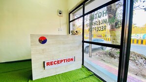Uma mesa de recepção com uma placa 'RECEPTION', uma tomada na parede e uma janela com vista para uma estrada e carros estacionados.