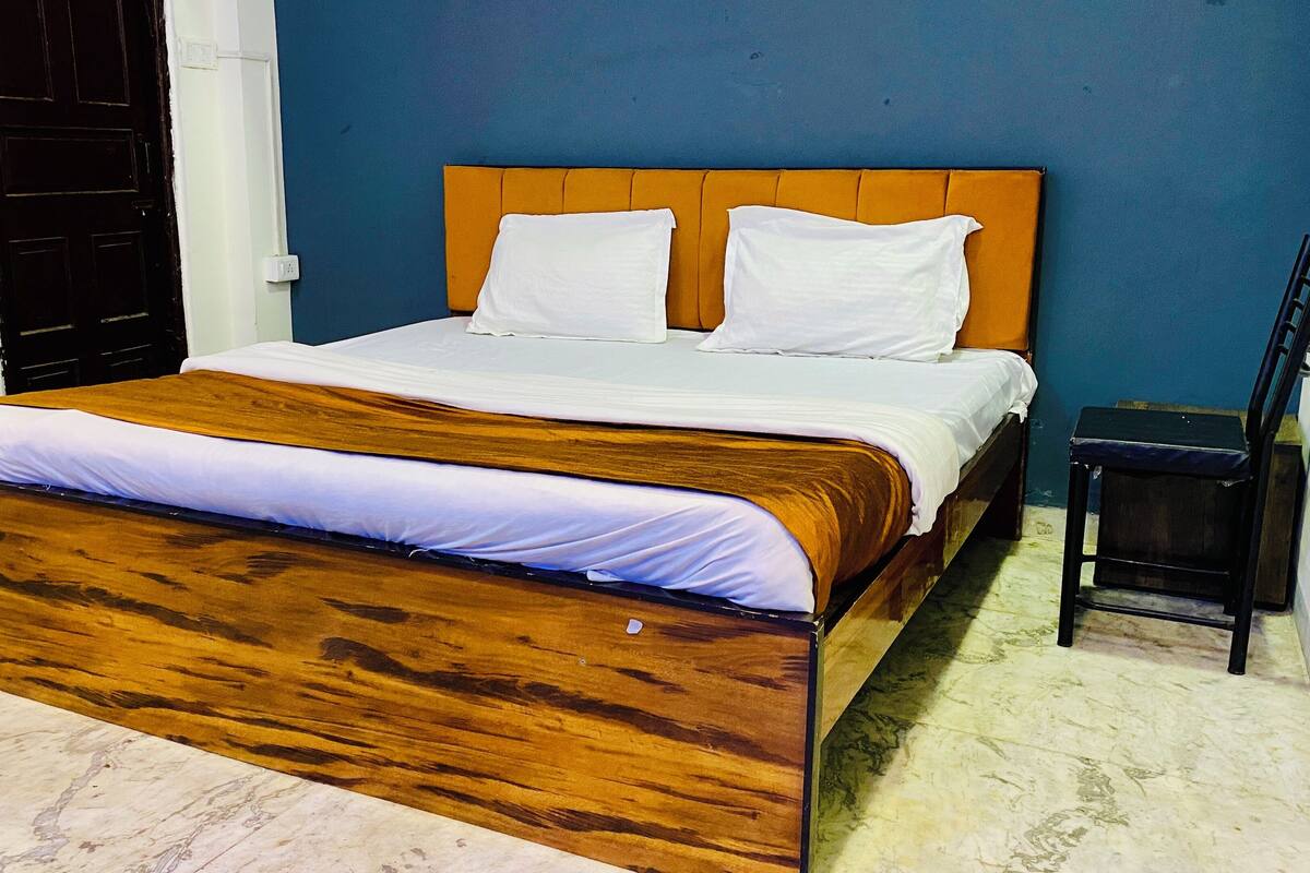 A bed with a wooden headboard and white bedding, a small table beside it, and a blue wall in the background.