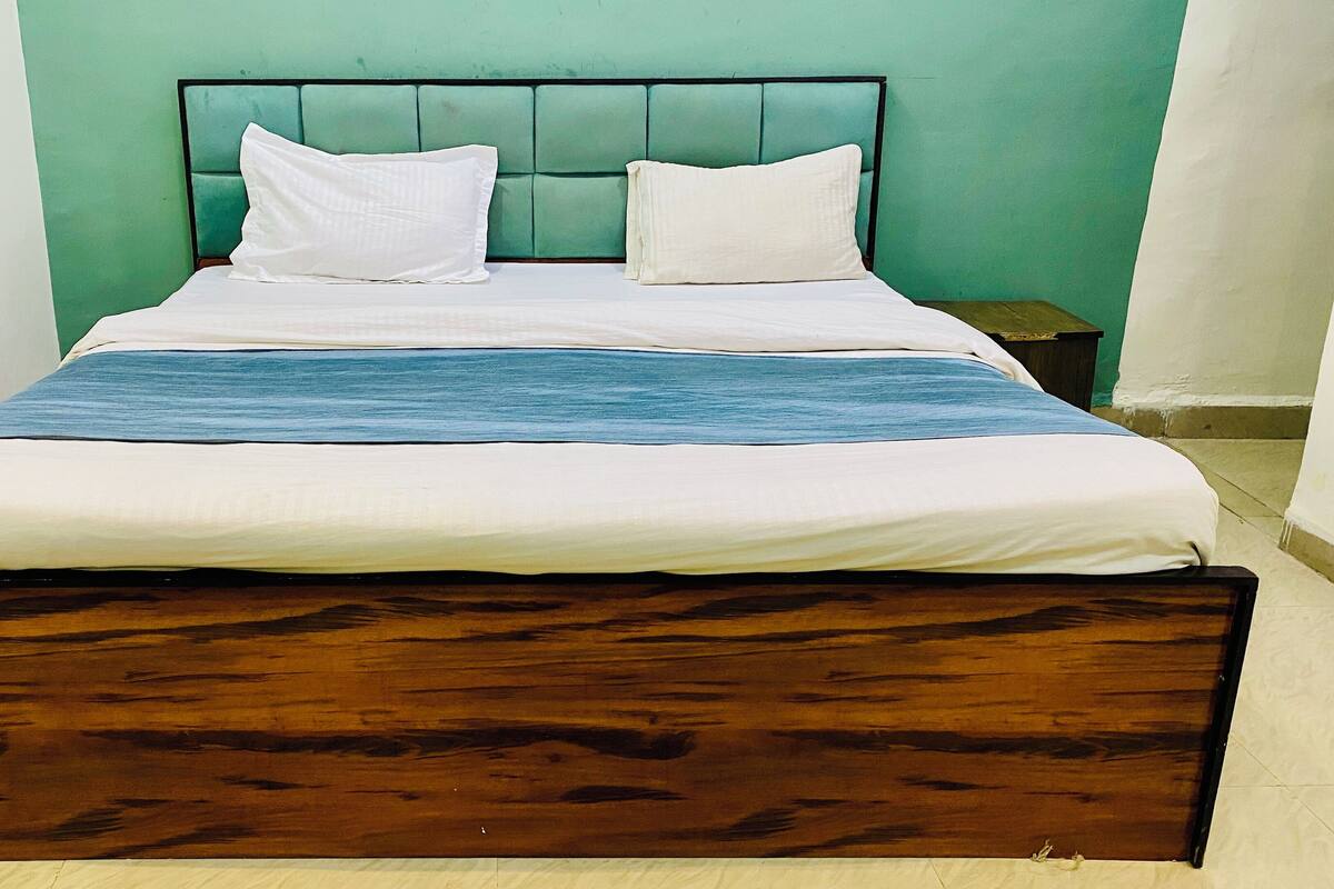 A bed with a wooden frame, two white pillows, a blue and white striped blanket, and a green wall behind it.