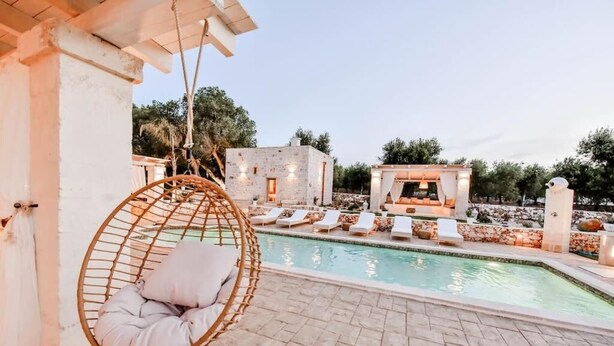 A pool area with a hanging chair, lounge chairs, and a stone building in the background. - Tenuta Maria Vittoria - Private pool & garden (Ostuni)