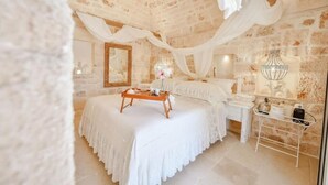 A bedroom with a stone wall, a bed with a white canopy, a bedside table, and a mirror. - Tenuta Maria Vittoria - Private pool & garden (Ostuni)
