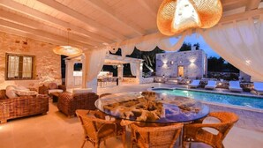 An outdoor dining area with wicker furniture and a glass table, overlooking a pool and stone building. - Tenuta Maria Vittoria - Private pool & garden (Ostuni)