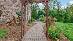 Un bâtiment en pierre surmonté d’une tonnelle en bois qui mène à un chemin pavé de briques.