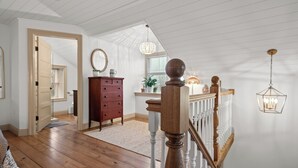 Une pièce spacieuse avec un plancher en bois, une commode en bois, un miroir et un luminaire suspendu.