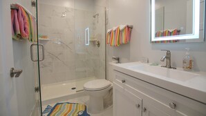 Un baño moderno con ducha de vidrio, inodoro y tocador con espejo.