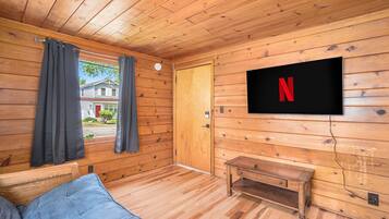 A cozy cabin room with wooden walls, a TV mounted on the wall, a bench, and a window with curtains.