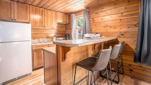 A kitchen with wooden cabinets, a white refrigerator, a sink, and a bar area with two chairs.