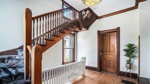 Una escalera de madera con baranda blanca, una puerta de madera con el número 2 y una planta en maceta.