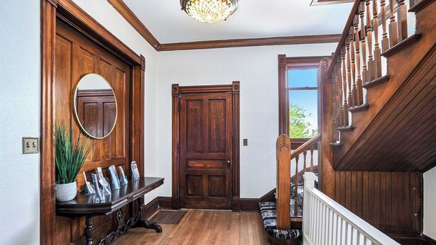 Una escalera de madera con barandilla, una puerta de madera y un espejo en la pared.